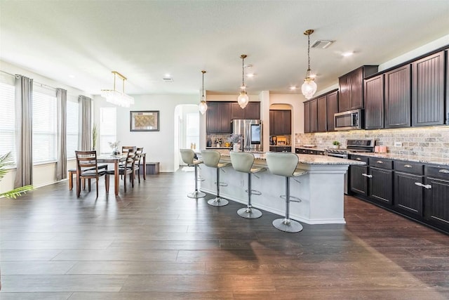 1224 Euless Ln, Leander, TX 78641 - kitchen featuring stainless steel appliances, arched walkways, a breakfast bar area, light stone countertops, and tasteful backsplash