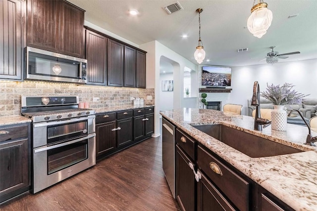 1224 Euless Ln, Leander, TX 78641 - kitchen featuring stainless steel appliances, a fireplace, arched walkways, dark wood finished floors, and decorative backsplash