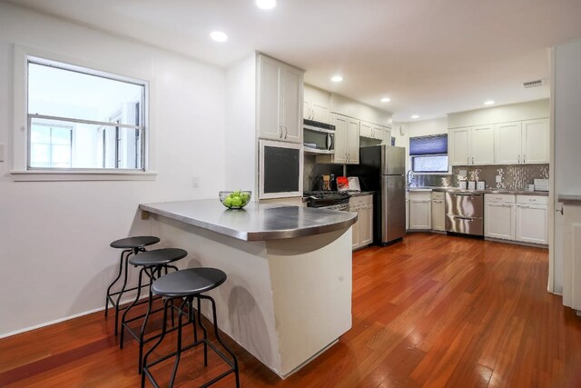 1005 Salem Ln, Austin, TX 78753 - kitchen with stainless steel counters, appliances with stainless steel finishes, a kitchen bar, dark wood-style floors, and recessed lighting