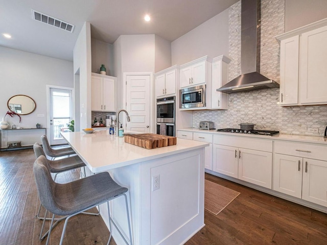 114 Loysoya St, Bastrop, TX 78602 - kitchen featuring wall chimney range hood, stainless steel appliances, white cabinetry, tasteful backsplash, and a breakfast bar area