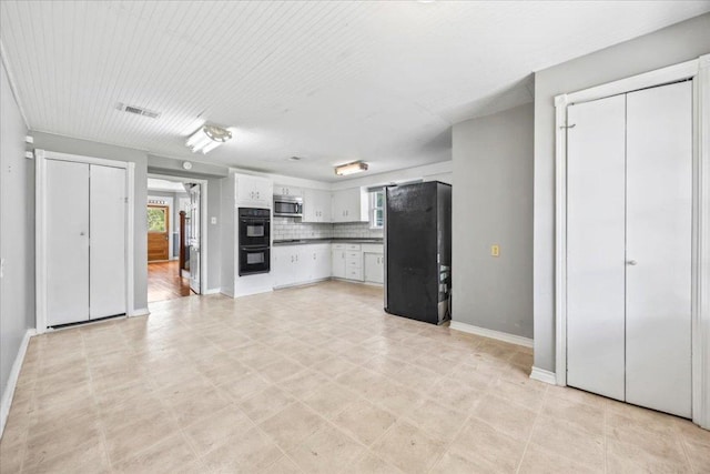 1223 Cecelia St, Taylor, TX 76574 - kitchen with stainless steel microwave, freestanding refrigerator, white cabinets, decorative backsplash, and baseboards