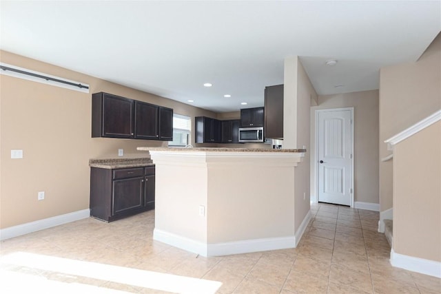 9001 Edmundsbury Dr, Austin, TX 78747 - kitchen with stainless steel microwave, light tile patterned flooring, baseboards, light countertops, and dark brown cabinets