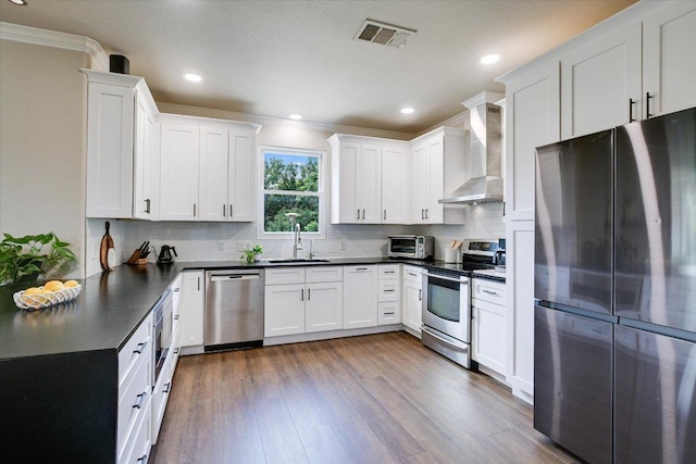 126 Whippoorwill Cir, Leander, TX 78641 - kitchen with appliances with stainless steel finishes, wall chimney exhaust hood, a sink, dark countertops, and ornamental molding