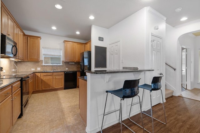 1813 Indian Lodge Dr, Cedar Park, TX 78613 - kitchen featuring black appliances, a breakfast bar area, arched walkways, backsplash, and dark stone counters