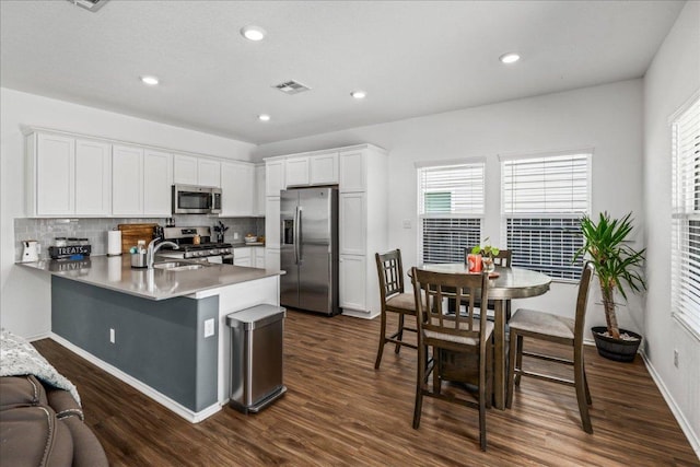 1725 Cobblecrest Ln, Leander, TX 78641 - kitchen with appliances with stainless steel finishes, a peninsula, dark wood finished floors, backsplash, and healthy amount of natural light