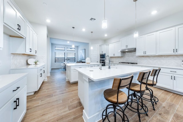 471 Diamondleaf Dr, Buda, TX 78610 - kitchen featuring an island with sink, under cabinet range hood, stainless steel microwave, gas cooktop, and light wood-style flooring