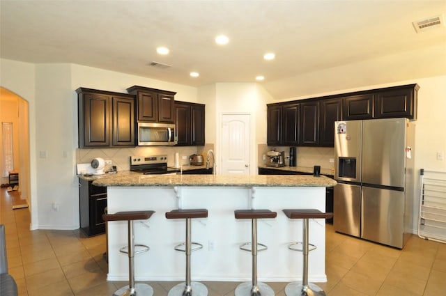 16805 Ruggio Rd, Pflugerville, TX 78660 - kitchen featuring appliances with stainless steel finishes, arched walkways, decorative backsplash, a kitchen breakfast bar, and an island with sink
