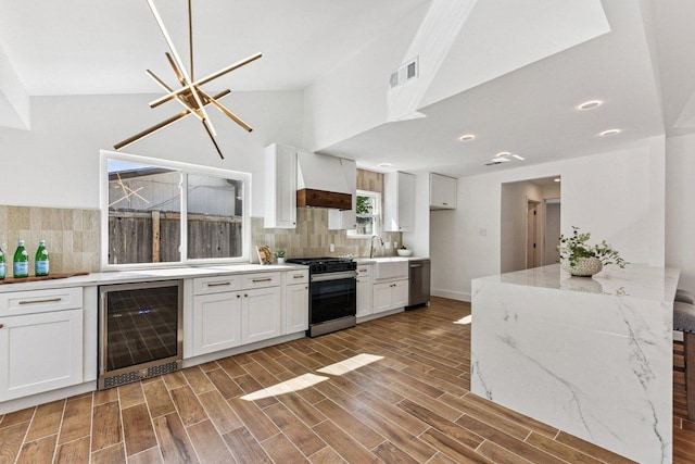 1111 Spearson Ln, Austin, TX 78745 - kitchen featuring beverage cooler, appliances with stainless steel finishes, white cabinetry, backsplash, and vaulted ceiling