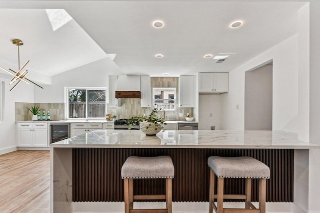 1111 Spearson Ln, Austin, TX 78745 - kitchen featuring wine cooler, backsplash, light stone counters, white cabinetry, and light wood-type flooring