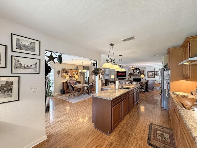 729 Trail Crest Dr, Canyon Lake, TX 78133 - kitchen featuring a fireplace, light wood-type flooring, open floor plan, black electric cooktop, and a chandelier