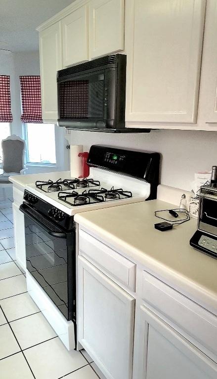 507 Dusty Leather Ct, Pflugerville, TX 78660 - kitchen featuring gas range, black microwave, white cabinets, light countertops, and light tile patterned floors