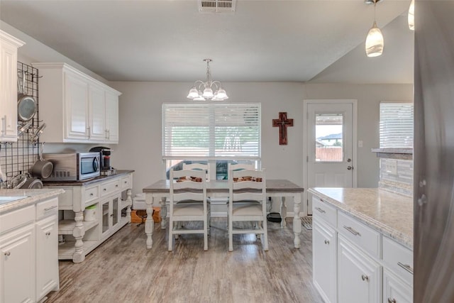 700 Indian Blanket St, Lockhart, TX 78644 - kitchen featuring light wood-style flooring, a chandelier, stainless steel microwave, white cabinets, and decorative backsplash