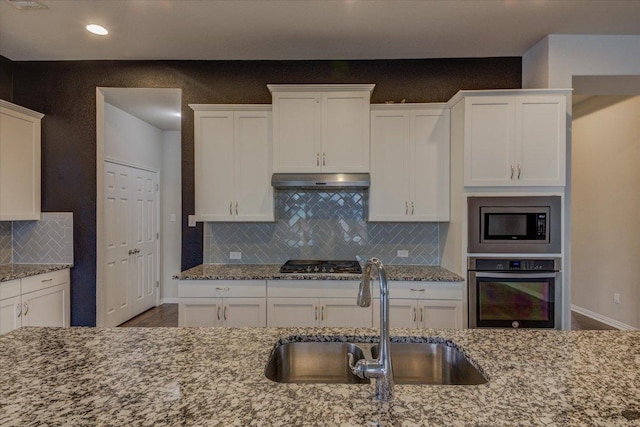 216 Allegrini St, Leander, TX 78641 - kitchen featuring appliances with stainless steel finishes, white cabinetry, light stone countertops, recessed lighting, and wood finished floors