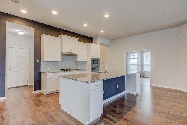 216 Allegrini St, Leander, TX 78641 - kitchen with stainless steel appliances, light wood-style flooring, under cabinet range hood, white cabinets, and a center island with sink
