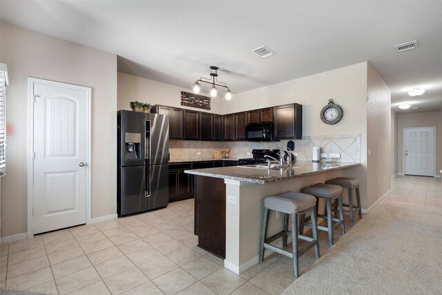 1407 Brashear Ct, Cedar Park, TX 78613 - kitchen featuring refrigerator with ice dispenser, black microwave, dark brown cabinetry, a breakfast bar, and decorative backsplash