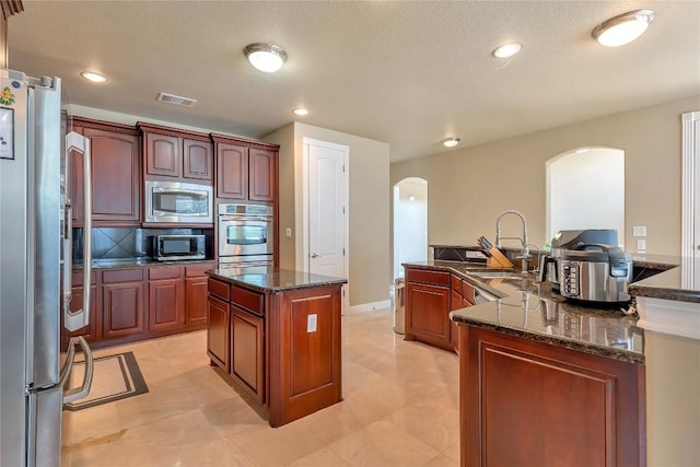 222 Vailco Ln, Austin, TX 78738 - kitchen with stainless steel appliances, arched walkways, a large island, dark stone countertops, and recessed lighting
