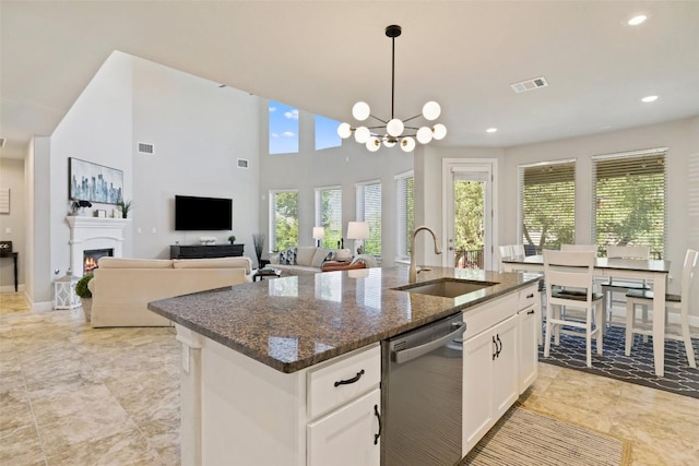 4225 Borho Ranch St, Leander, TX 78641 - kitchen with dishwasher, dark stone counters, a kitchen island with sink, white cabinetry, and a lit fireplace