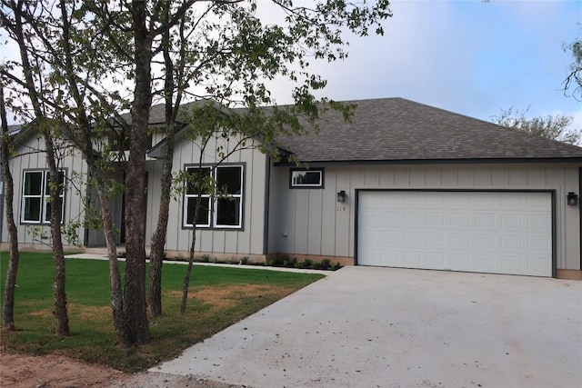119 Waimanalo Dr, Bastrop, TX 78602 - single story home featuring a shingled roof, concrete driveway, board and batten siding, a garage, and a front yard