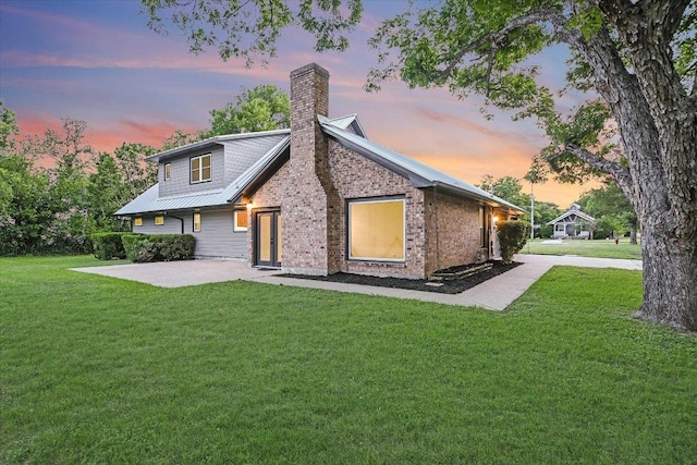 503 Elm St, Bastrop, TX 78602 - back of house at dusk with a patio, a yard, a chimney, a metal roof, and brick siding