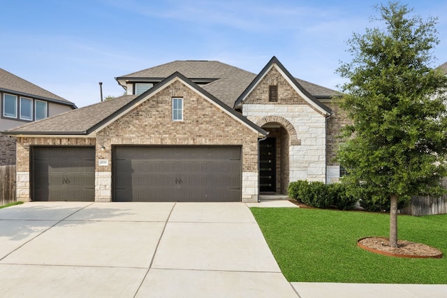 1816 Arapaho Mountain Pass, Leander, TX 78641 - french country home featuring a garage, stone siding, concrete driveway, a shingled roof, and brick siding