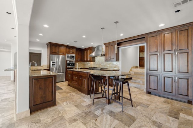 10810 River Terrace Cir, Austin, TX 78733 - kitchen featuring stainless steel appliances, wall chimney exhaust hood, light stone countertops, decorative backsplash, and a kitchen breakfast bar