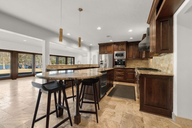 10810 River Terrace Cir, Austin, TX 78733 - kitchen featuring appliances with stainless steel finishes, wall chimney range hood, stone tile floors, recessed lighting, and backsplash