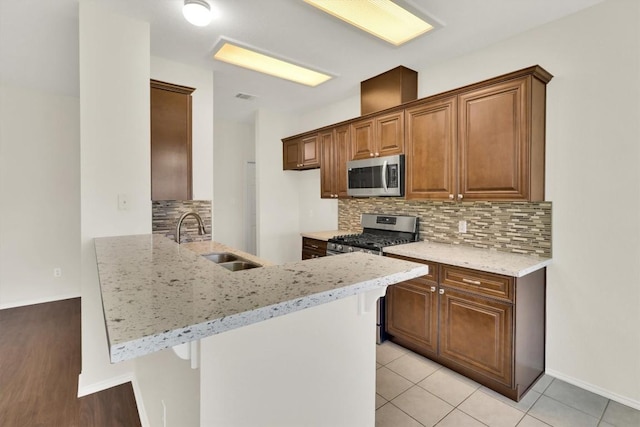 1718 Zydeco Dr, Round Rock, TX 78664 - kitchen with appliances with stainless steel finishes, a peninsula, backsplash, light stone counters, and light tile patterned floors