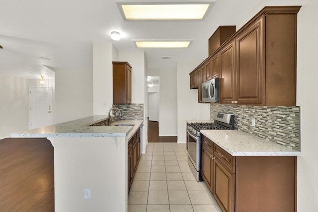 1718 Zydeco Dr, Round Rock, TX 78664 - kitchen with appliances with stainless steel finishes, a peninsula, decorative backsplash, light stone counters, and a breakfast bar area