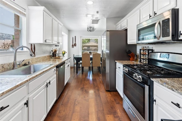 1424 Roxannes Run, Pflugerville, TX 78660 - kitchen featuring appliances with stainless steel finishes, white cabinets, dark wood-style floors, a textured ceiling, and light stone counters