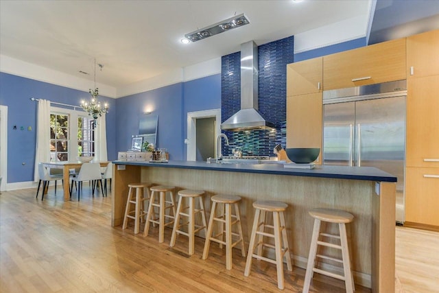 2109 Nickerson St, Austin, TX 78704 - kitchen featuring wall chimney exhaust hood, built in fridge, a breakfast bar area, light wood-type flooring, and decorative backsplash