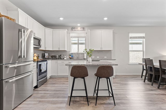 1925 T H Johnson Dr, Taylor, TX 76574 - kitchen featuring stainless steel appliances, a breakfast bar, light stone countertops, tasteful backsplash, and white cabinets