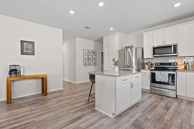 1925 T H Johnson Dr, Taylor, TX 76574 - kitchen with stainless steel appliances, light wood-style floors, a kitchen island, white cabinets, and a kitchen bar