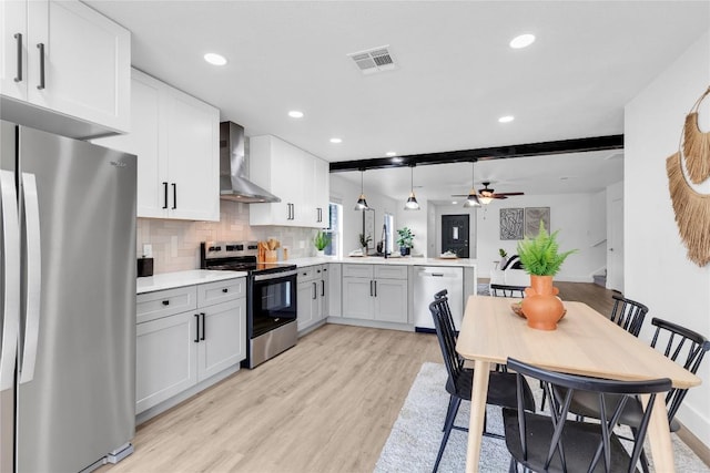 111 Woodley Rd, Leander, TX 78641 - kitchen featuring appliances with stainless steel finishes, wall chimney exhaust hood, a peninsula, light wood-style floors, and light countertops