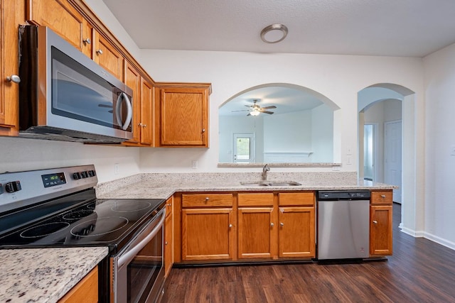 18111 Gallant St, Manor, TX 78653 - kitchen with stainless steel appliances, dark wood-style floors, ceiling fan, brown cabinets, and light stone counters
