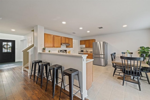 216 Prairie Verbena Dr, Kyle, TX 78640 - kitchen featuring freestanding refrigerator, under cabinet range hood, white microwave, a kitchen breakfast bar, and light countertops