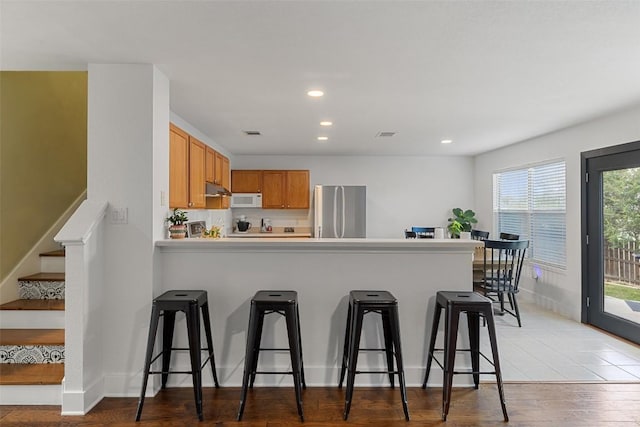 216 Prairie Verbena Dr, Kyle, TX 78640 - kitchen with freestanding refrigerator, white microwave, a peninsula, under cabinet range hood, and light wood-style flooring