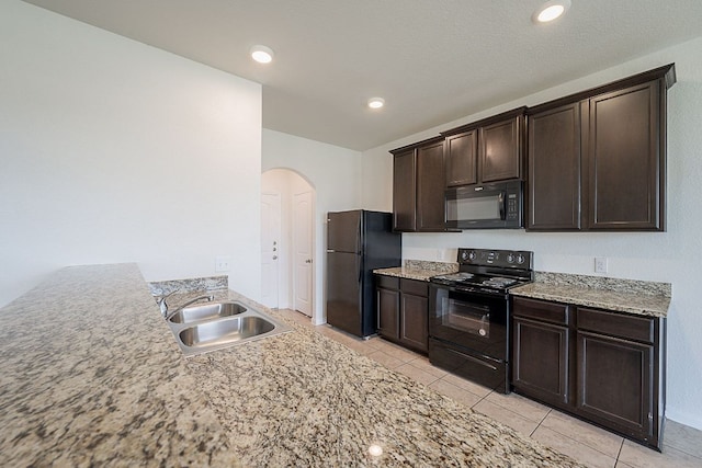 20016 Woodrow Wilson St, Manor, TX 78653 - kitchen featuring black appliances, arched walkways, dark brown cabinetry, light tile patterned floors, and light stone counters