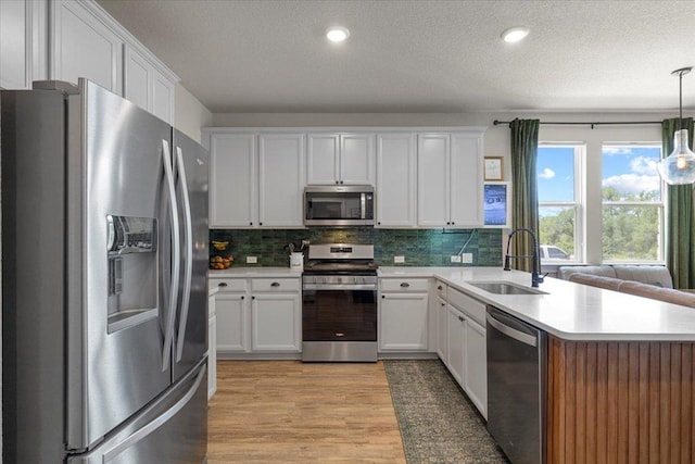 496 Sawtooth Mountain Way, Dripping Springs, TX 78620 - kitchen with stainless steel appliances, light wood-style floors, backsplash, light countertops, and a textured ceiling