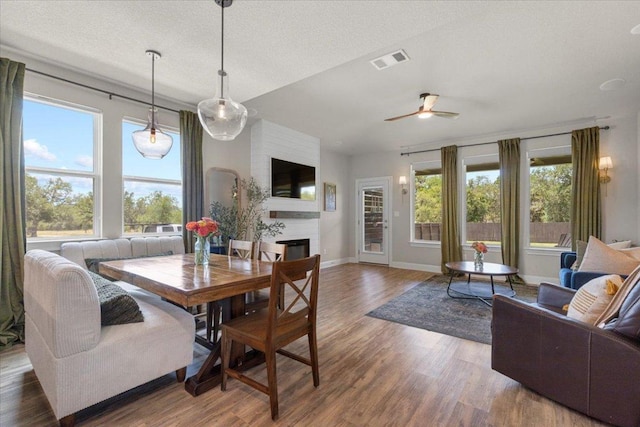 496 Sawtooth Mountain Way, Dripping Springs, TX 78620 - dining space with a fireplace, wood finished floors, plenty of natural light, a ceiling fan, and a textured ceiling