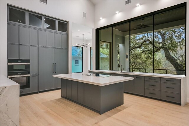 5217 S Scout Island Cir, Austin, TX 78731 - kitchen featuring gray cabinetry, black appliances, light wood finished floors, light countertops, and a towering ceiling