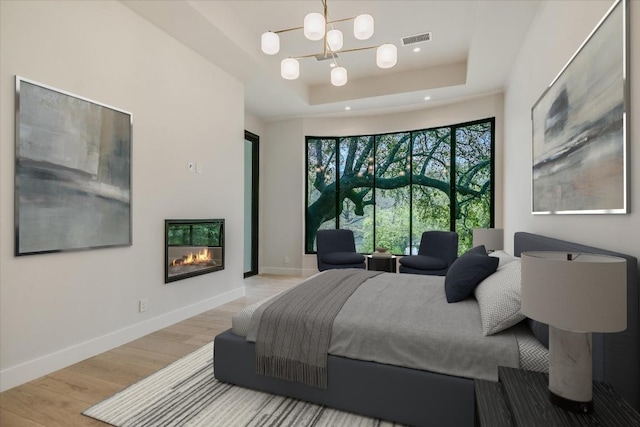 5217 S Scout Island Cir, Austin, TX 78731 - bedroom featuring a tray ceiling, wood finished floors, a chandelier, and a glass covered fireplace