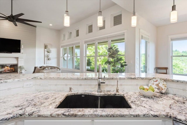2501 Woodbine Cir, Georgetown, TX 78628 - kitchen featuring open floor plan, light stone counters, a glass covered fireplace, and a ceiling fan