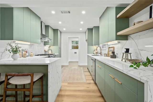 2114 Vanderbilt Ln, Austin, TX 78723 - kitchen with green cabinetry, wall chimney exhaust hood, light wood-type flooring, backsplash, and recessed lighting