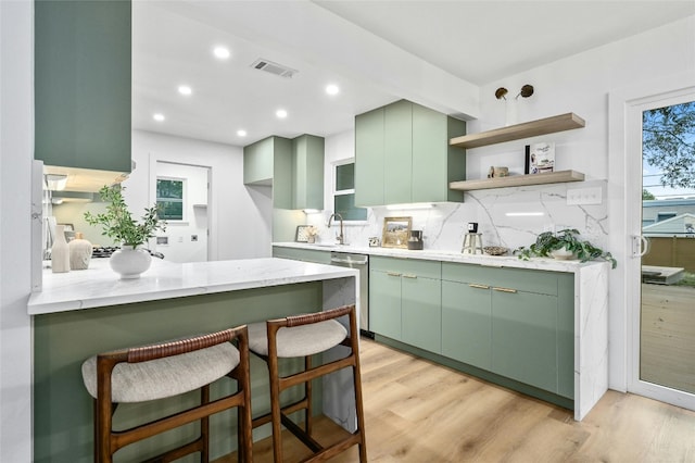 2114 Vanderbilt Ln, Austin, TX 78723 - kitchen featuring green cabinets, stainless steel dishwasher, backsplash, a breakfast bar, and light wood-style floors