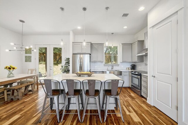 10129 Longhorn Skwy, Dripping Springs, TX 78620 - kitchen with gray cabinets, appliances with stainless steel finishes, a breakfast bar, decorative backsplash, and wood finished floors