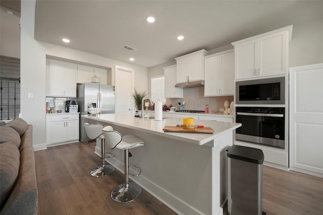 1113 Spring Gulch Ln, Georgetown, TX 78628 - kitchen featuring under cabinet range hood, appliances with stainless steel finishes, a kitchen bar, dark wood-type flooring, and recessed lighting