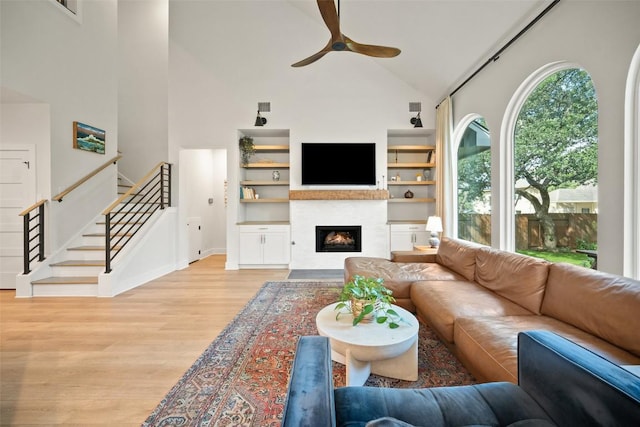 7308 Black Mountain Dr, Austin, TX 78736 - living room with high vaulted ceiling, a ceiling fan, light wood-style floors, a glass covered fireplace, and stairs