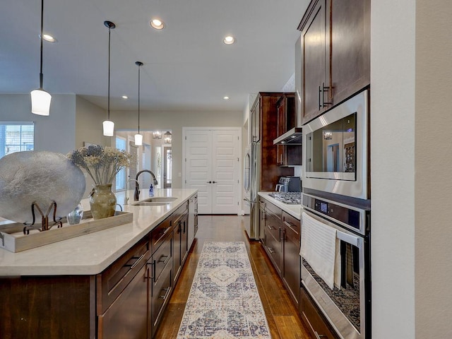 217 Skipping Cedar St, San Marcos, TX 78666 - kitchen with appliances with stainless steel finishes, a kitchen island with sink, dark brown cabinetry, dark wood-style flooring, and recessed lighting