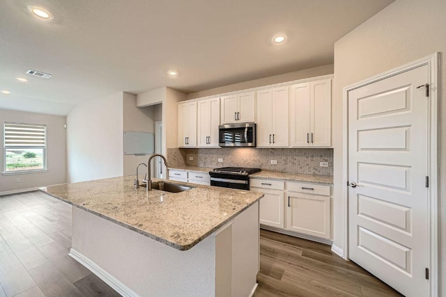 2871 Mill Run Bnd, Round Rock, TX 78665 - kitchen featuring stainless steel microwave, black range with gas cooktop, dark wood-style floors, white cabinets, and decorative backsplash