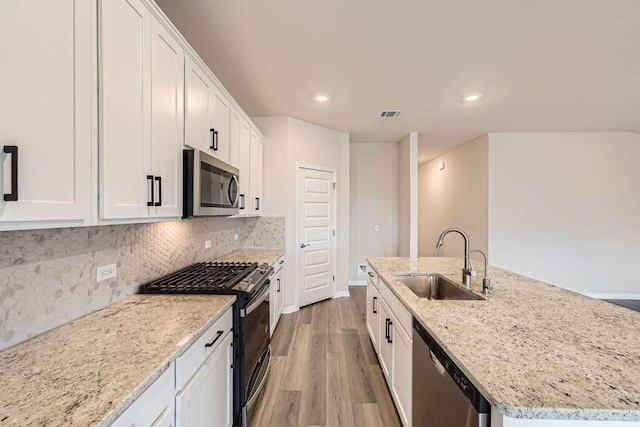 2871 Mill Run Bnd, Round Rock, TX 78665 - kitchen with appliances with stainless steel finishes, a center island with sink, light wood finished floors, white cabinets, and decorative backsplash